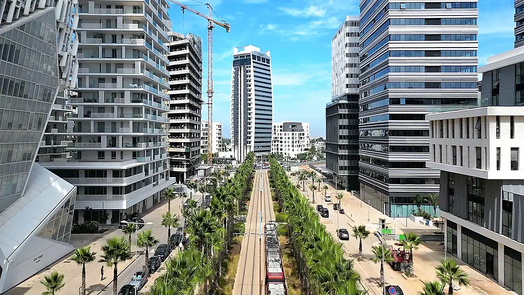 A wide boulevard lined with palms and new office towers, a tram line down its centre and a tower crane on the skyline